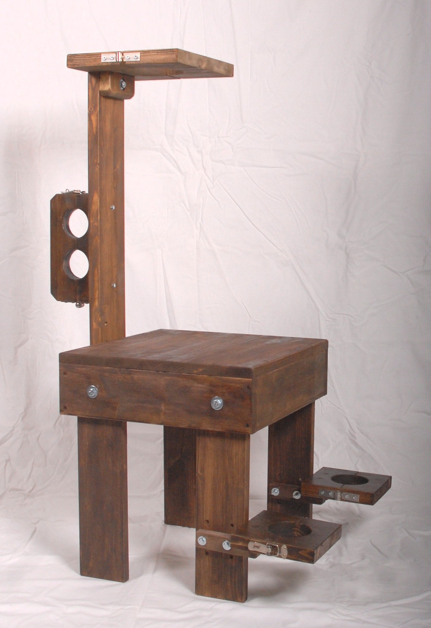 Walnut-stained wooden interrogation chair with bondage restraints.