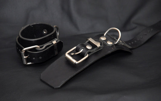 Black leather bondage wrist cuffs with roller buckle and D-ring.