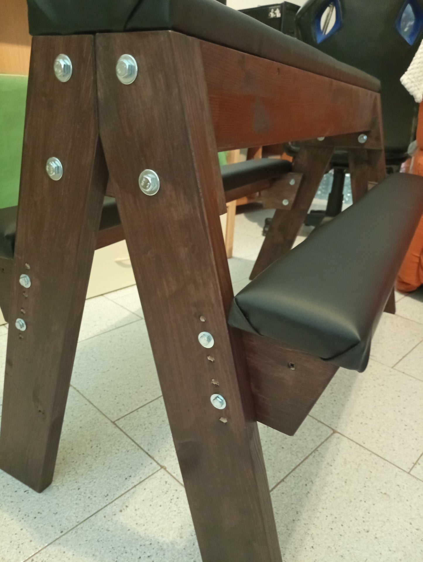 Wooden spanking bench featuring height-adjustable side supports and padded central surface.